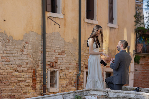 Man proposing to woman on a Venice bridge, seen from behind.