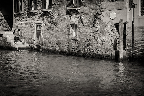 Black and white shot of couple sitting by a Venetian canal during engagement session.