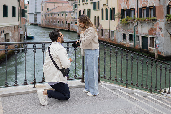 A man kneels on one knee to propose on a quiet bridge in Cannaregio, Venice.