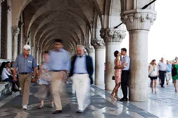 Blurred crowd walking past a couple under Venetian arches