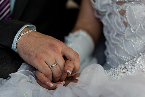 Close-up of bride and groom holding hands, showing their wedding rings.