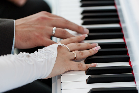 Bride's hands on piano keys, playing a melody during the wedding.