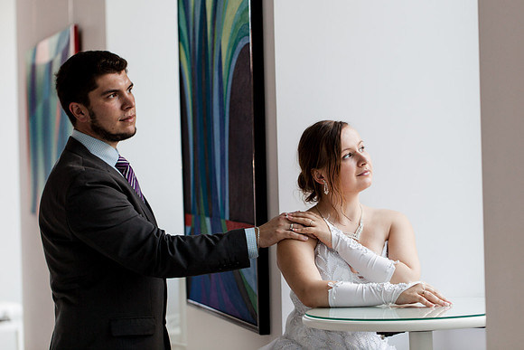 Bride and groom standing in a modern art gallery, reflecting.
