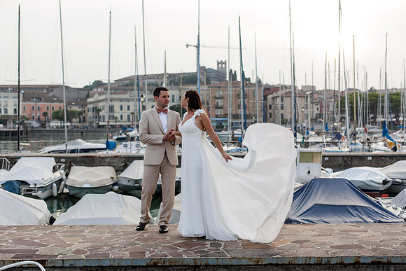 Bride and groom standing by the marina, boats in the background.