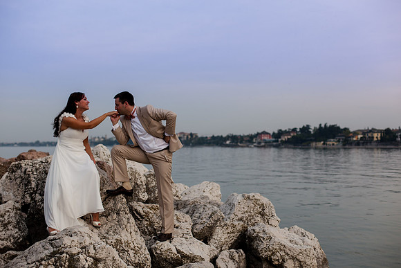 Bride and groom sitting on rocks, embracing with a scenic water view.