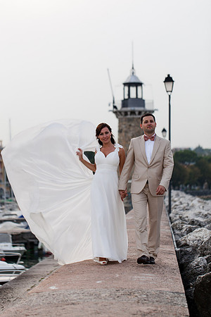 Bride and groom under a flowing veil by the sea.
