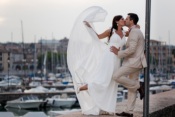 Bride and groom with veil flowing near the marina.