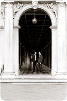 Engaged couple walking under historic Venetian archways in black and white.