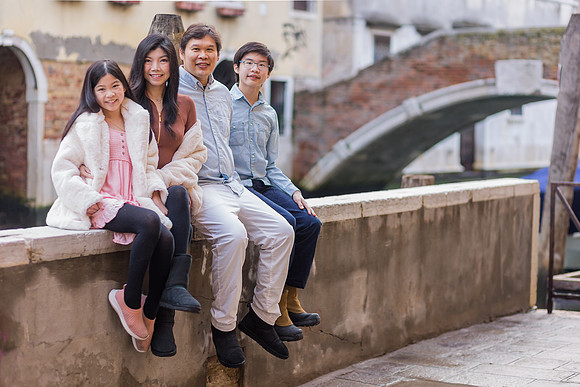 Family of four standing on a stone bridge in Venice, winter season.
