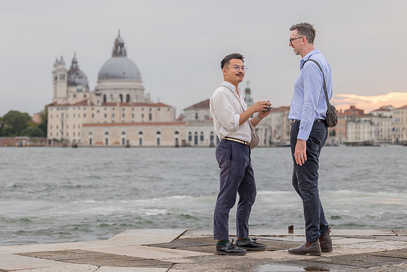 Gay couple standing together while one holds the engagement ring box.