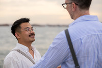 Close up of engaged gay couple laughing together by the water.