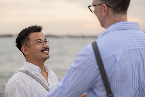 Close up of engaged gay couple laughing together by the water.