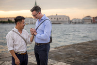 Gay couple holding hands by the water during golden hour in Venice.