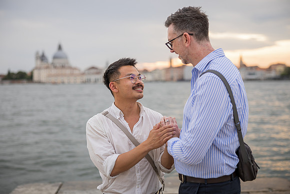 Couple crouching by the lagoon edge smiling at each other.