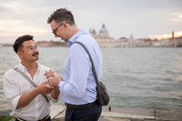Engaged men looking deeply at each other by the water.