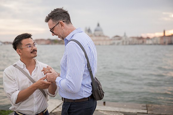 Engaged men looking deeply at each other by the water.