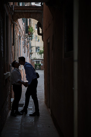 Silhouetted gay couple kissing under an archway in Venice.