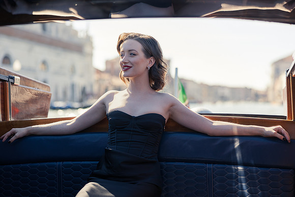 Actress Sunny Mittmann smiling in a wooden water taxi heading to the Excelsior Hotel.