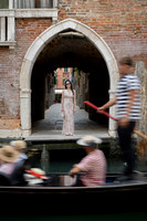 Woman standing under a brick archway with a passing gondola in Venice.