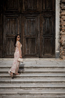 Woman in a light dress standing on stairs in front of large wooden doors.