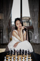 Woman sitting elegantly next to a chessboard in a beautifully lit room.