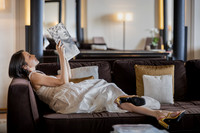 Woman lying on a couch reading a magazine in a luxury hotel room.