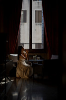 Woman looking out of a window in a dimly lit historic room.
