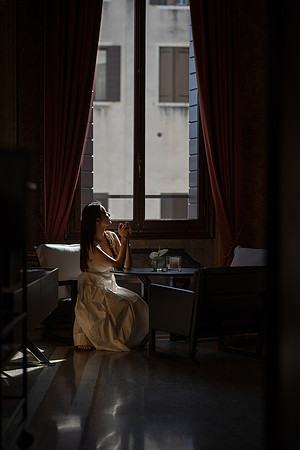 Woman looking out of a window in a dimly lit historic room.