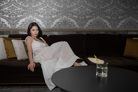 Woman in a white dress sitting on a large dark sofa in a modern room.