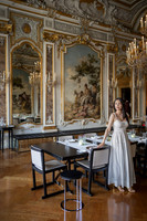 Woman in a ballroom surrounded by ornate mirrors and golden decorations.