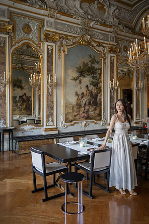Woman in a ballroom surrounded by ornate mirrors and golden decorations.