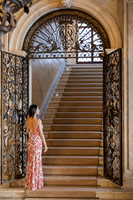 Woman walking up a grand stone staircase with ornate metal railings.