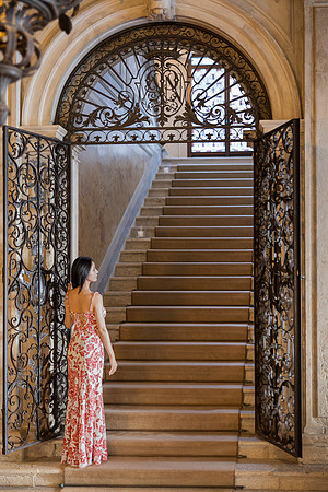 Woman walking up a grand stone staircase with ornate metal railings.