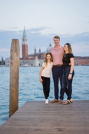 Family posing by the water with gondolas in the background during their family photo session in Venice