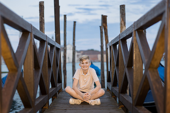 Daughter sitting by the water surrounded by wooden piers in Venice during a family vacation