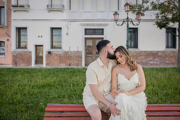 Engaged couple sitting close together on a red bench in Venice.