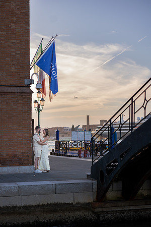 Venetian flag waving at sunset near a historic staircase.