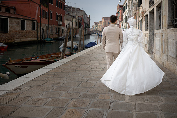 Couple walking along a Venetian canal, wedding dress flowing.