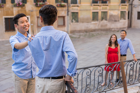 Family standing by a Venetian railing with historic buildings in the background.