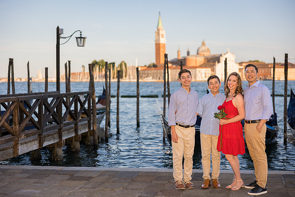 Three generations family portrait by the water in Venice, with gondolas and the skyline behind them.