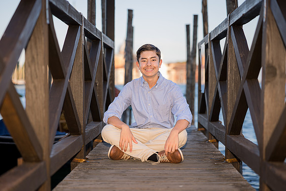 Son sitting on a wooden pier in Venice, enjoying the view of gondolas and water during the family session.