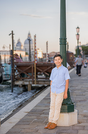 Son standing by the Venetian waterfront, with gondolas and city skyline in the background.