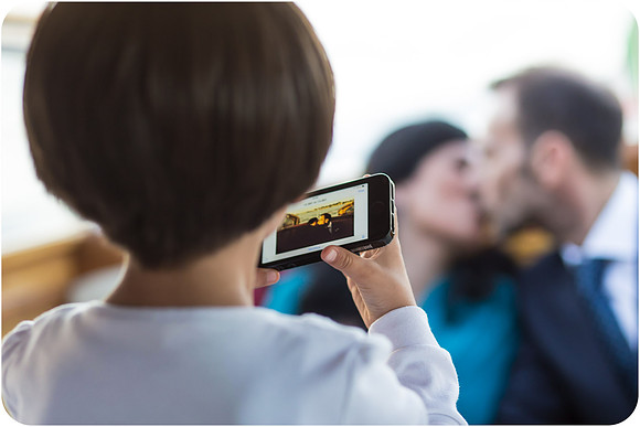 Child taking a photo of the bride and groom kissing during the wedding day in Venice.