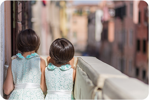 Two sisters in blue dresses looking over the canal in Venice during a wedding.