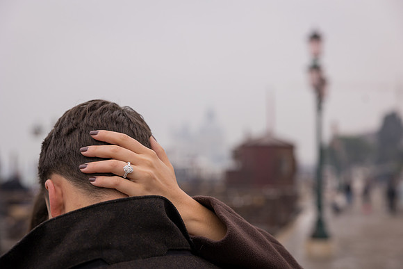 Couple hugging near docked gondolas in Venice, engagement ring visible.