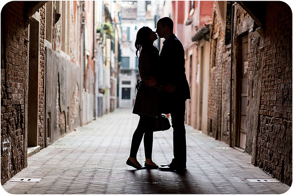 Couple standing in the shadows of a historic arch in Venice