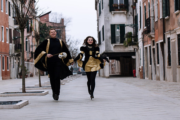 Masked couple in black and gold carnival attire dancing in Venice.