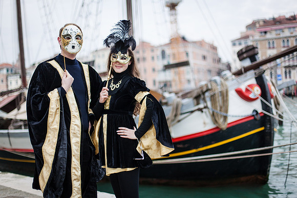 Masked couple in Venice with the lagoon and gondolas behind them.