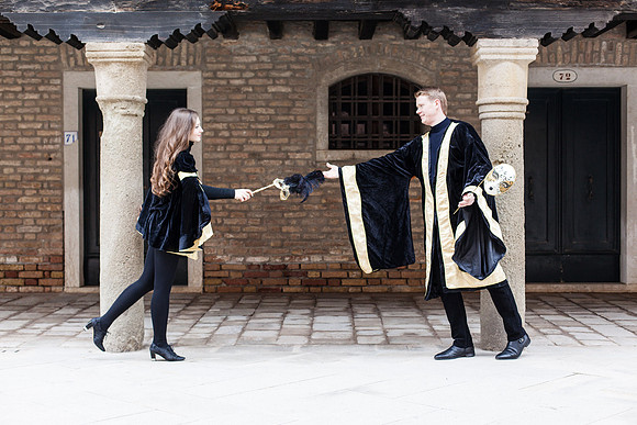 Masked couple standing in a historic Venetian courtyard.