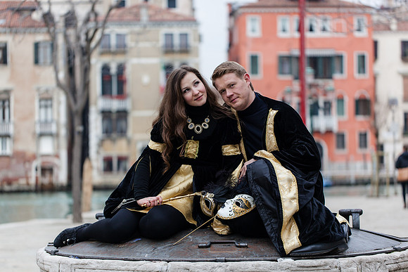 Venetian couple in carnival masks embracing by the Grand Canal.